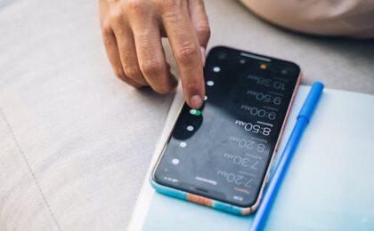 Close-up of a hand touching a smartphone with a blue case and a pen nearby.